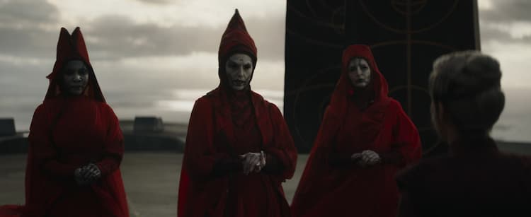 Three Nightsister witches dressed in red gowns talk with Morgan Elsbeth in the foreground