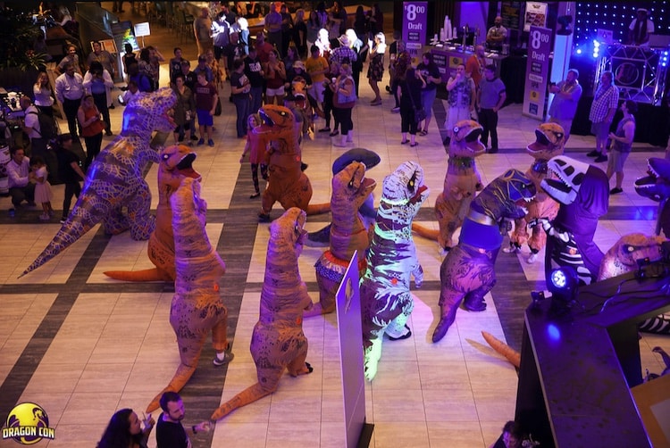 Crowds watching a group of a dozen people wearing inflatable T-rex costumes.