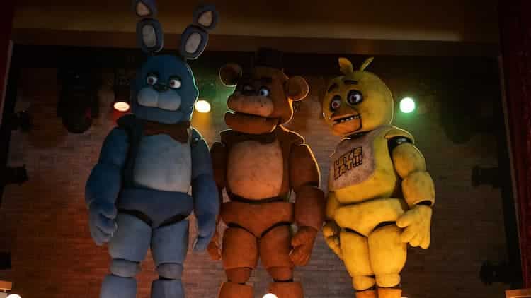 Bonnie, Freddy, and Chica are staring to the left. They're standing on the stage with a brick wall and multi-coloured lights behind them