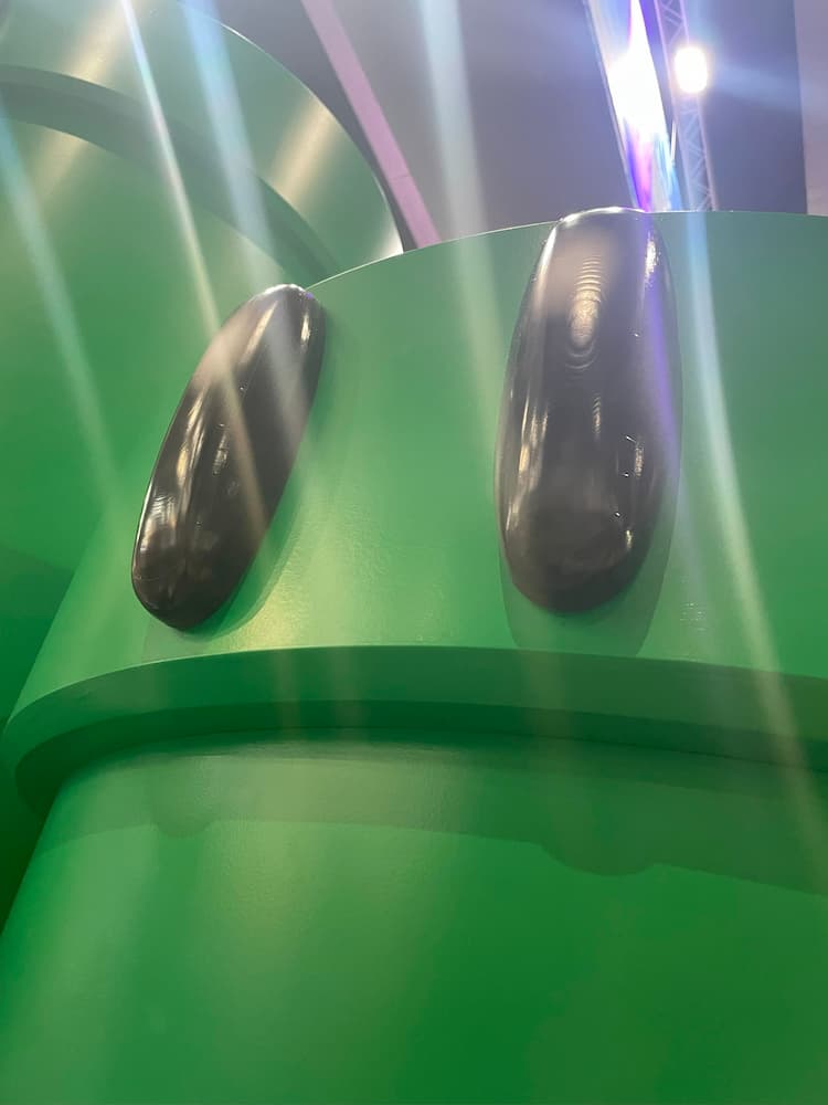 A green warp pipe with eyes. Rays of light are shining down on the green pipe.