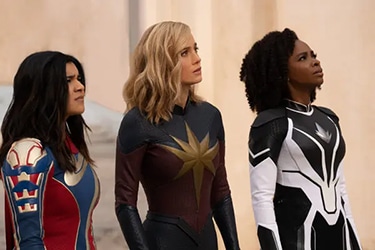 Kamala, Carol, and Monica are standing together. They are all looking towards the sky with worried looks on their faces.