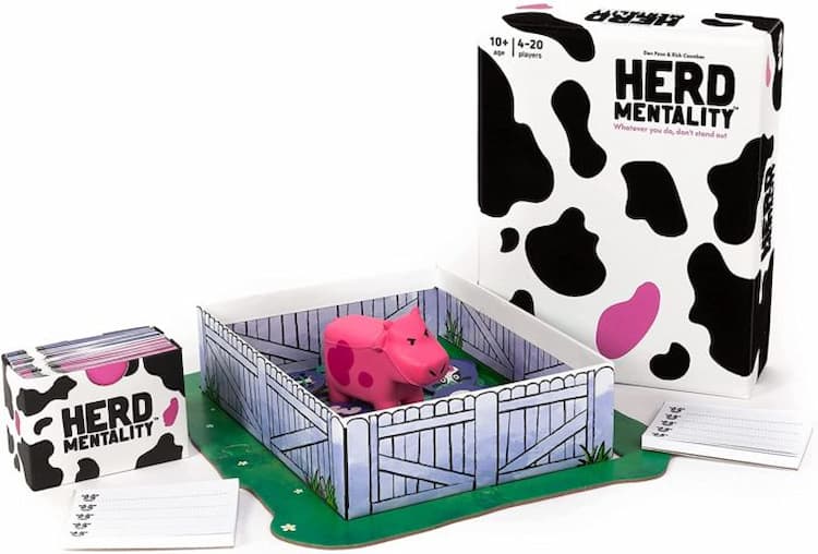 An angry pink cow is in the middle of a small paddock. A set of Herd Mentality game cards is on the left and the game box is on the right.