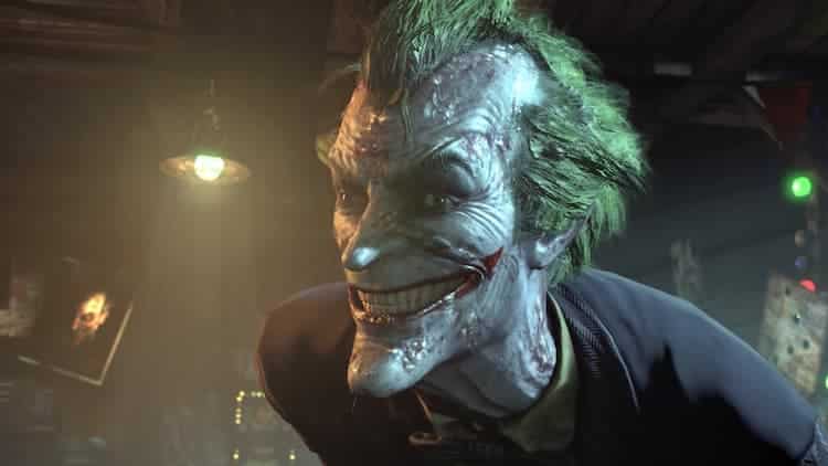 Joker is smiling. His eyes are looking in two different directions. He looks unwell, with his right eye being half red. A light is on behind him as well as a painting of himself.