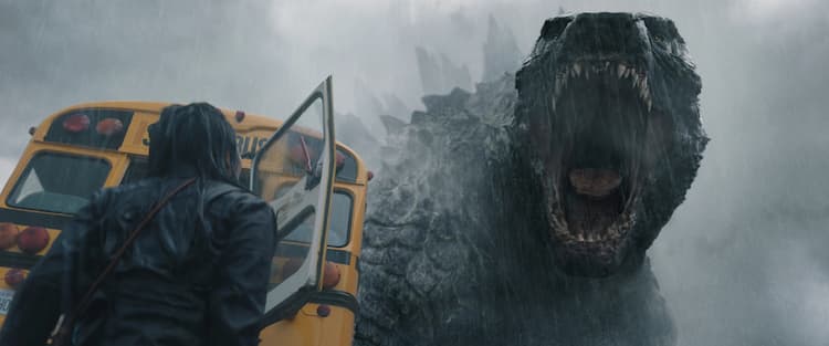 Godzilla is roaring in the rain. Cate is looking at Godzilla. A yellow school bus with its back door open is in front of Cate.