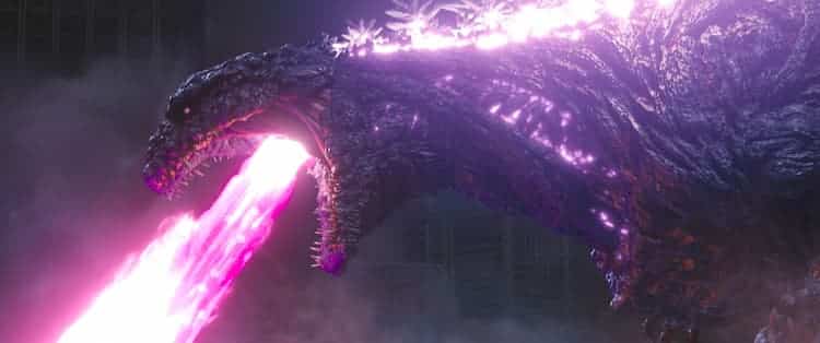 Godzilla is shooting his atomic breath. The beam is a purple colour. The spines on his back are glowing purple. Smoke is covering the bottom left corner.