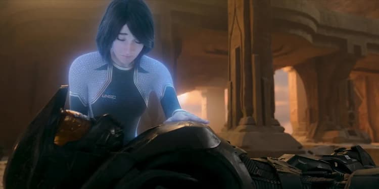 Cortana has her hand on the chest armour of Master Chief. Cortana has her eyes closed and her head lowered. They are in a desert temple with pillars behind them.