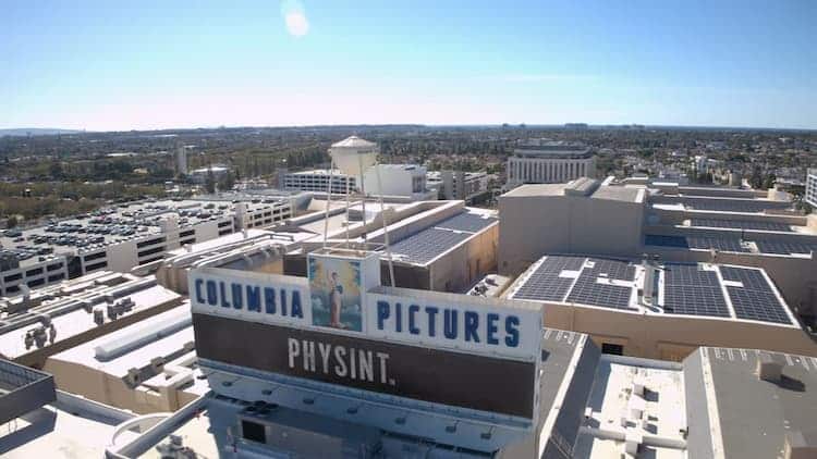 A large building with the words Columbia Pictures. Underneath it, there's the word "Physint". The sky is clear and blue. Various smaller buildings surround the big one.