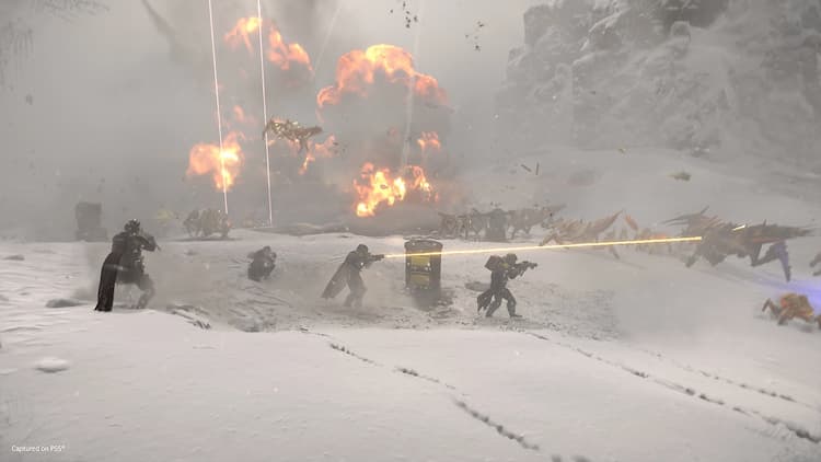 A screenshot of an in-game mission where a squad of four helldivers face off against a swarm alien bugs with explosions in the background.