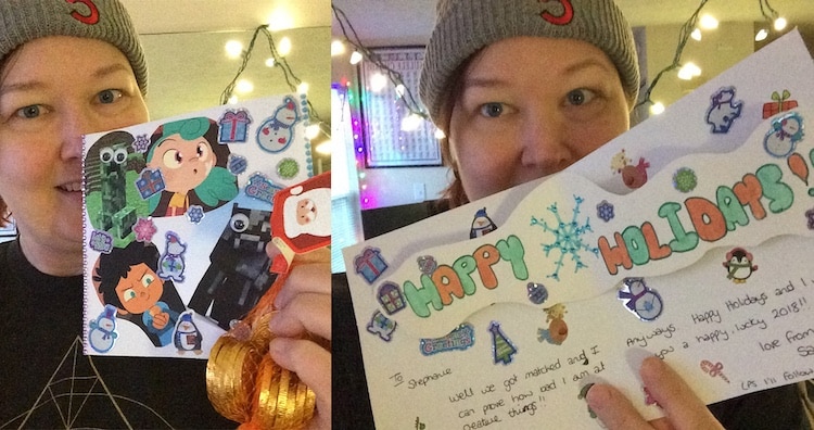 Stef Watson holding up a hand-made holiday card featuring holiday stickers and images from Rooster Teeth productions.