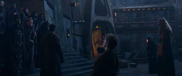 Indara is walking in front of Aniseya's coven. The coven are on the stairs and Indara and the other Jedi are at the bottom. The other Jedi include Torbin, Kelnacca, and Sol. They are in the middle of a courtyard at night.