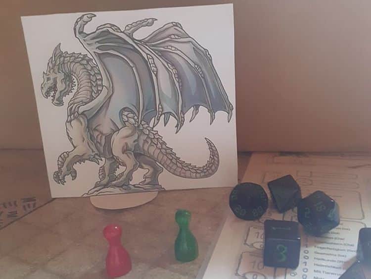 Play pieces are spread out on a Dungeons and Dragons map with art of a Bronze Dragon printed on a piece of paper looming over them