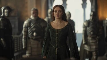 Olivia Cooke stands as Alicent Hightower in a green dress with a look of concern. Her guards are behind her.